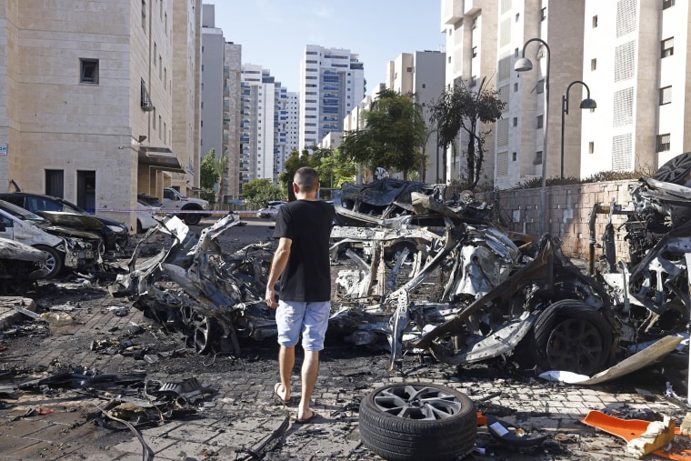 A person walks burned cars and destruction in an apartment complex parking lot