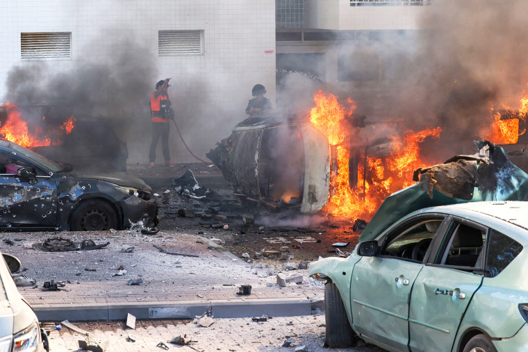 Emergency personnel spray water on burning cars engulfed in flames following a rocket attack