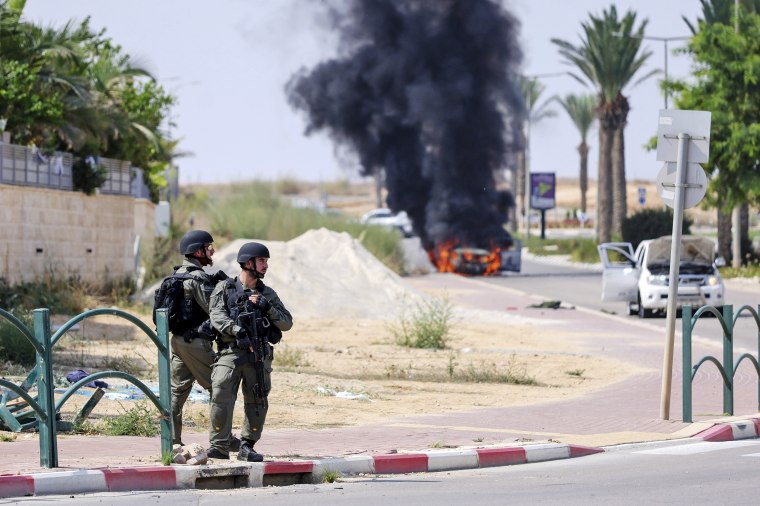 Israeli soldiers take position in the southern Israeli town of Ofakim on Sunday, Oct. 8, 2023. Hamas militants stormed over the border fence Saturday, killing hundreds of Israelis in surrounding communities. The burning car was used by the gunmen and set on fire by the residents. 