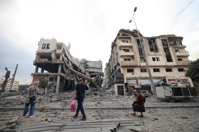 Palestinians carrying personal belongings walk past heavily damaged buildings following Israeli airstrikes on Gaza City's al-Rimal district