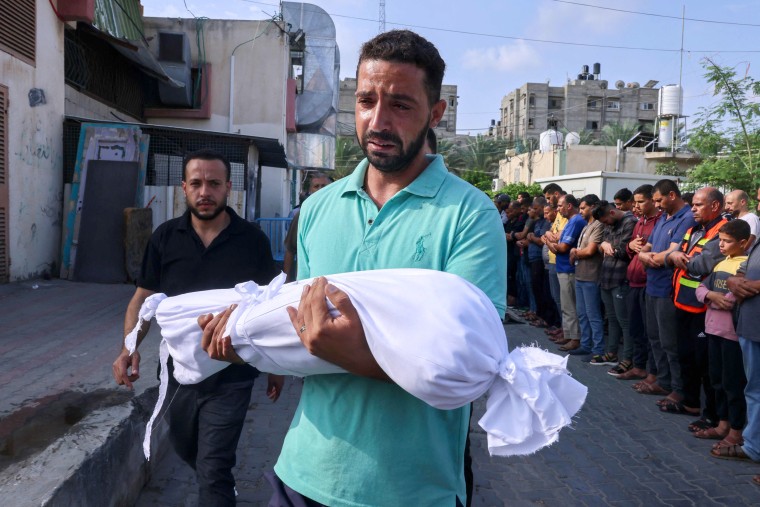 A Palestinian man carries the body of a child killed in overnight Israeli shelling