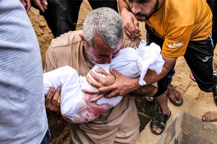 A man cries as he holds the wrapped body of a child.