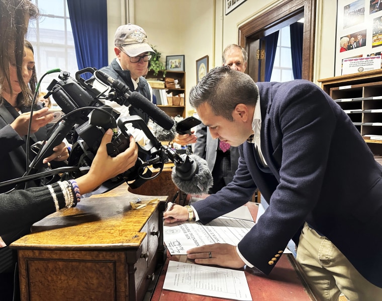 Reporters watch John Anthony Castro signs a poster after filing to get on the Republican ballot for the New Hampshire primary