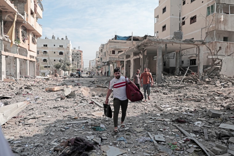 People walk through rubble and debris along a destroyed street while evacuating Gaza City