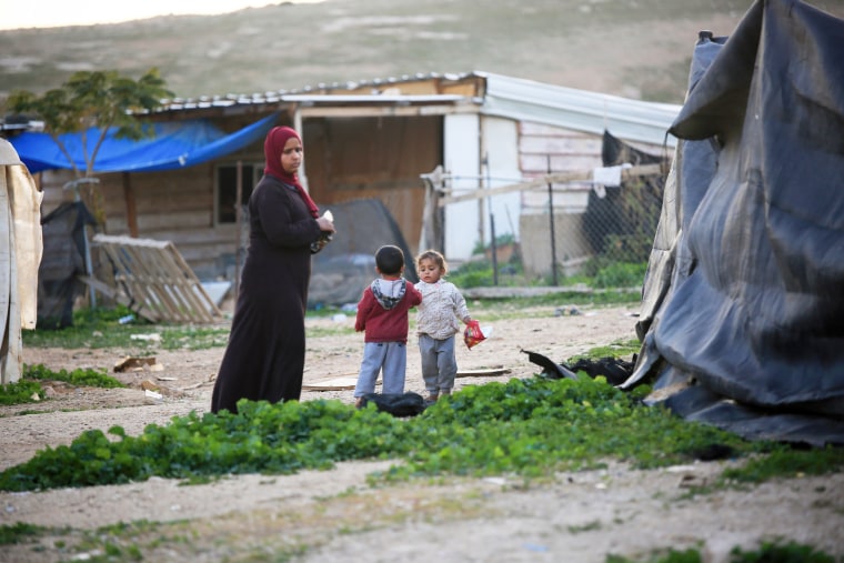 Children play next to a woman in the village of Khan al-Ahmar