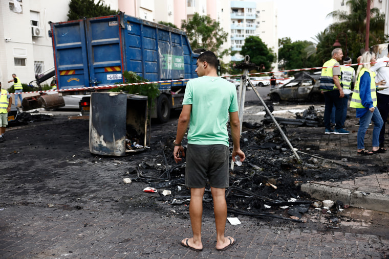 An Israeli civilian looks at destroyed cars. 