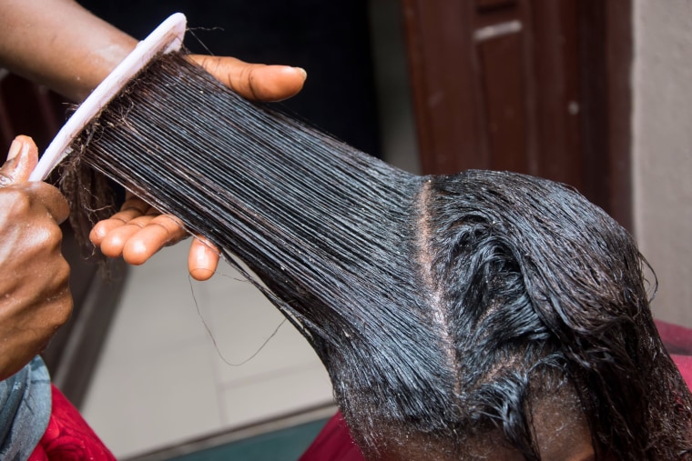 A hairdresser uses a comb to apply a cream relaxer in the hair