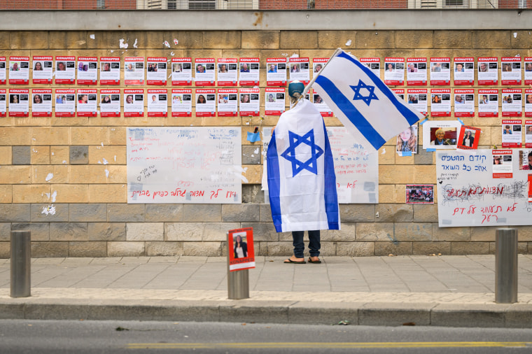 A person wrapped in an Israeli flag looks at photographs of some of those taken hostage by Hamas  in Tel Aviv on Oct. 18, 2023.