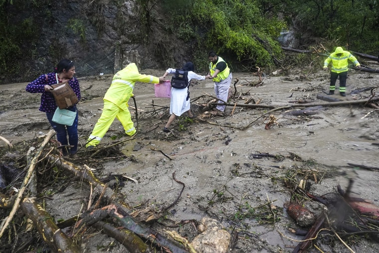 Image: People get help crossing a highway blocked by a landslide triggered by Hurricane Otis 