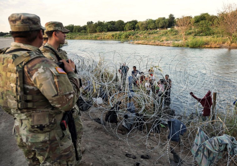 Members of the National Guard look on as migrants try to find a way past razor wire