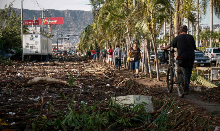 People walk next to debris left after the passage of Hurricane Otis in Acapulco, Mexico