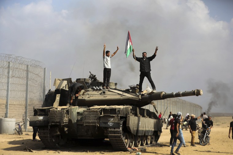 Palestinos celebran junto a un tanque israelí destruido en la valla que separa Gaza de Israel el 7 de octubre.