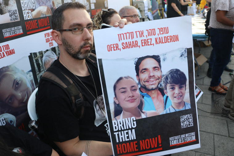 Eyal Kalderon, 38, holds a sign with photos of his loved ones, Ofer, Sahar and Erez Kalderon.