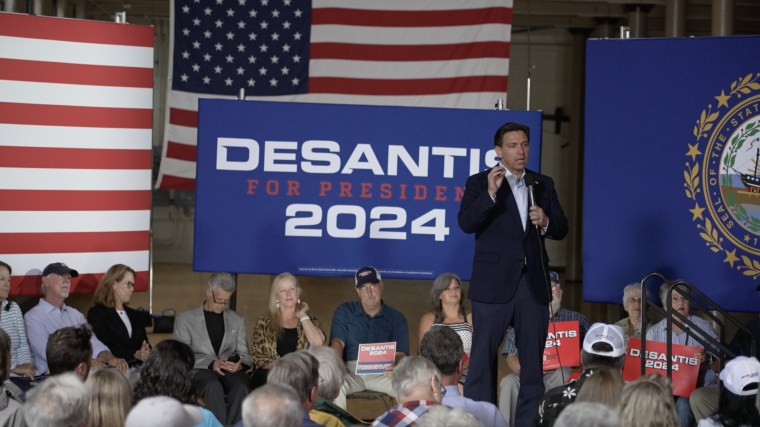 Ron DeSantis speaks at a Never Back Down-hosted event, with super PAC signage and logos behind him.