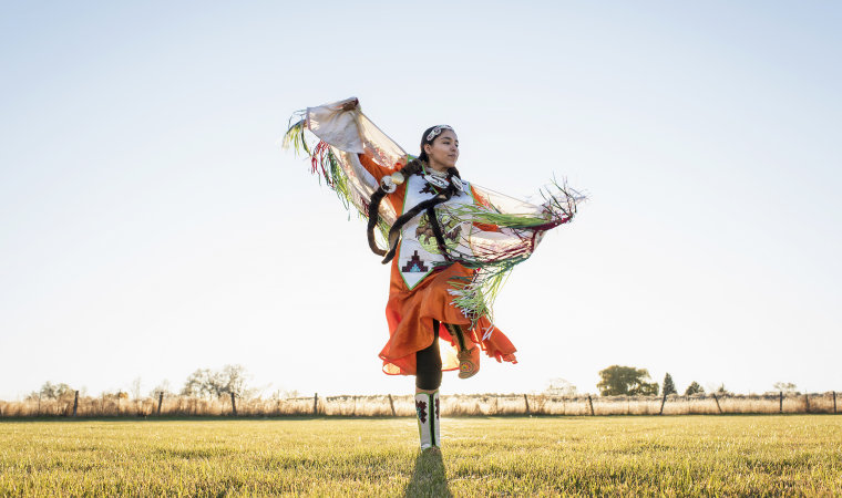 Young Native American woman dancing in traditional dress.