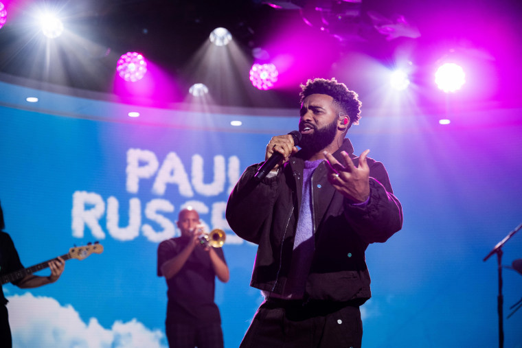 Paul Russell holds a mic on a TV studio set and sings.