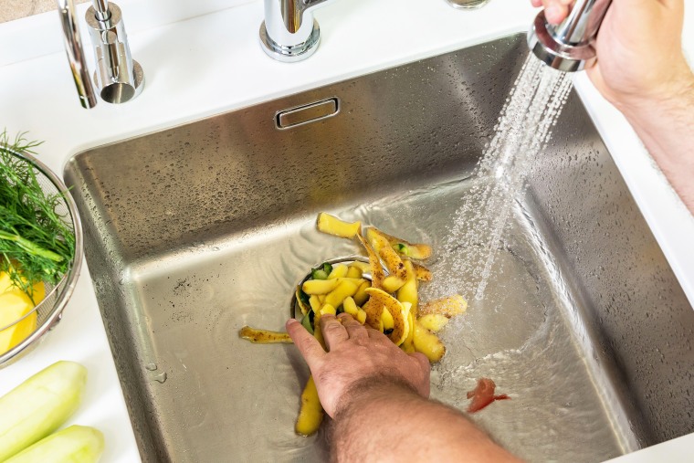 Putting food waste in the sink garbage disposer.