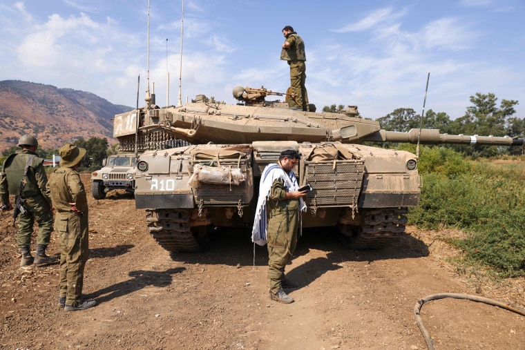 An Israeli soldier prays in front of a tank
