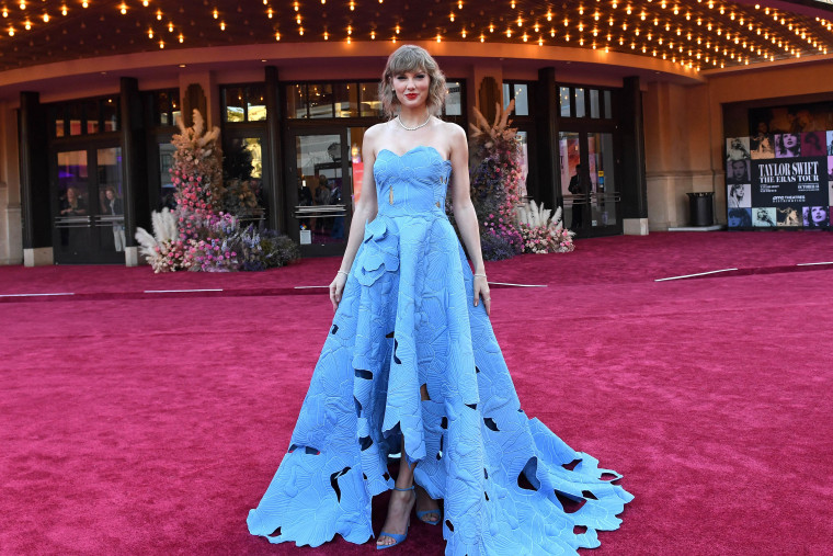 Swift stands on a red carpet in front of a movie theater in a blue floral dress.