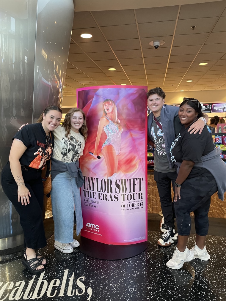 A group of young people pose in front of a Taylor Swift poster