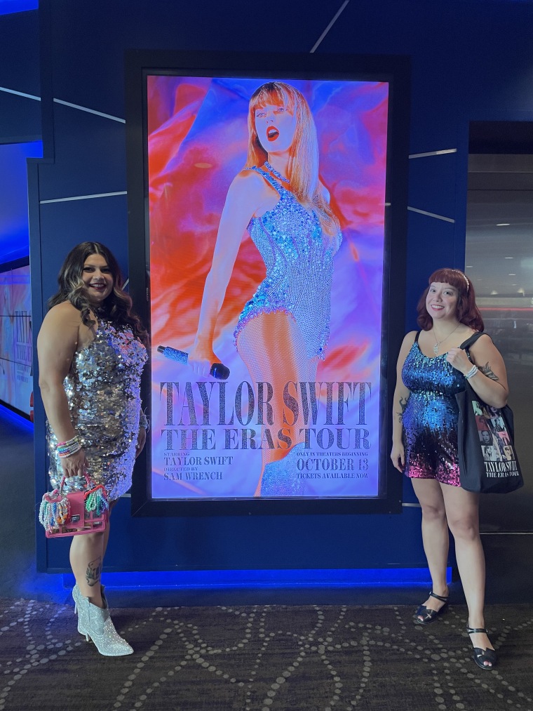 Two women pose in front of a Taylor Swift poster