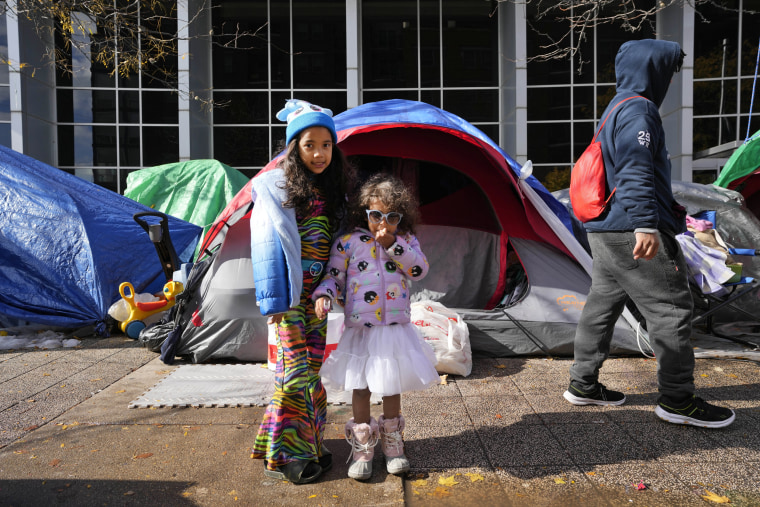 Immigrant sisters Arantza, left, and Antonella wear Halloween costumes next to a small community of migrant tents, Wednesday, Nov. 1, 2023, near the Northside Police Station in Chicago. 