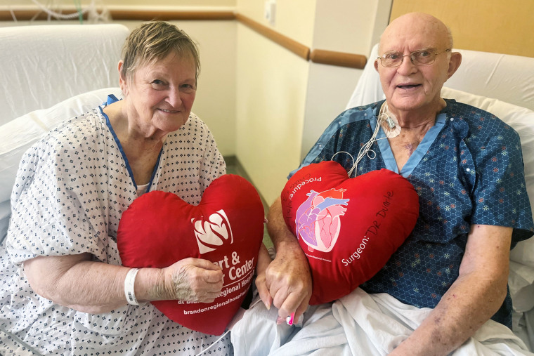 Phil and Margaret Vaske hold hands and heart-shaped pillows in a hospital room.