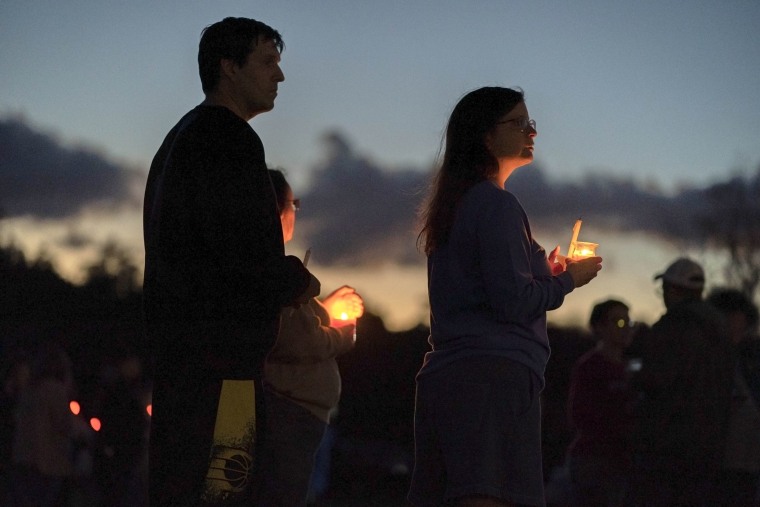 People hold candles during a vigil at sunset.