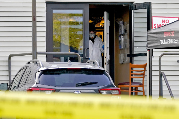 A person in a hazmat exits the Schemengees Bar & Grille, with yellow caution tape in the foreground