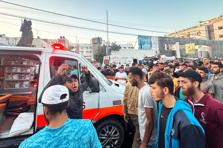 A person shouts to a crowd as people gather around an ambulance damaged in a reported Israeli strike in Gaza