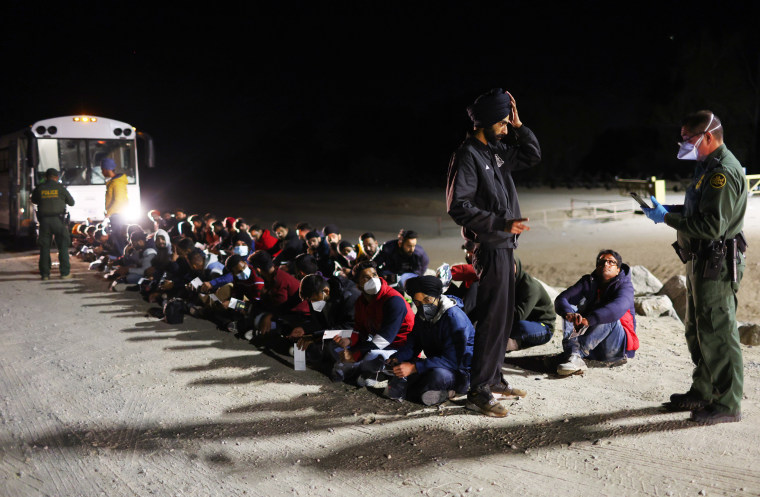 Migrants from India wait to board a bus to be taken for processing after crossing the border from Mexico