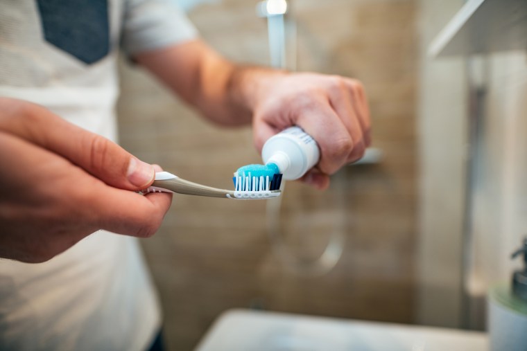 Person squeezing toothpaste onto a toothbrush.