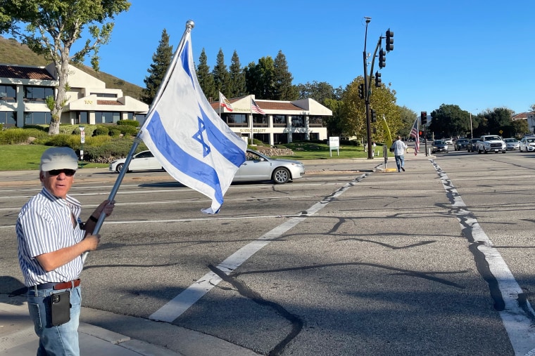 A man waves an Israeli flag in a park space on a city street