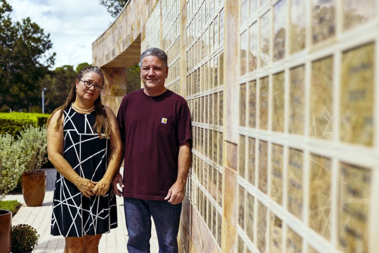Elena Martinez and Jaime Mejia in front of a columbarium memorial where their son’s ashes are interred at St. Agnes Catholic Church in Naples, Fla.