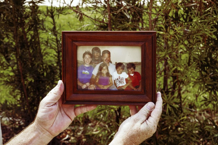 Jaime Mejia holds a photo of him and his children, including Sebastian, standing behind the couch. 