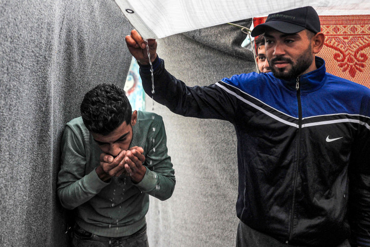 Men use their hands to drink rainwater dripping from the roof of a tent at a U.N.-run school in Gaza.