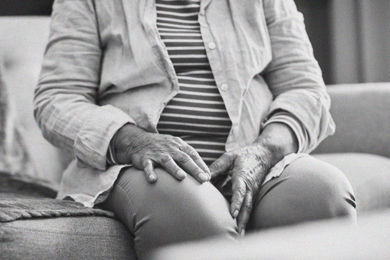 Image: A senior Black woman touching her leg while sitting.