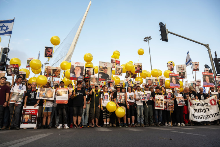 People with yellow balloons and signs with photos of the hostages held by Hamas stand in a street