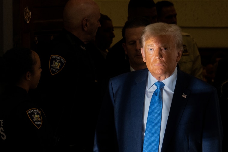 Light illuminates half of Donald Trump's face as he's surrounded by a phalanx of court security personnel.