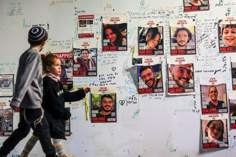 Image: Children walk past portraits of Israeli hostages posted on a wall in Tel Aviv