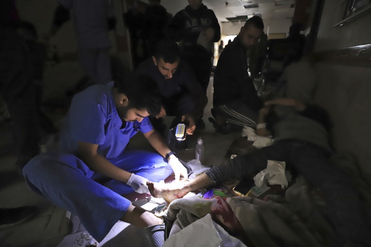 A man shines a flashlight so a Palestinian medic can treat a wounded person after power ran out at the Indonesian Hospital in Beit Lahiya, Gaza, on Nov. 19, 2023. 
