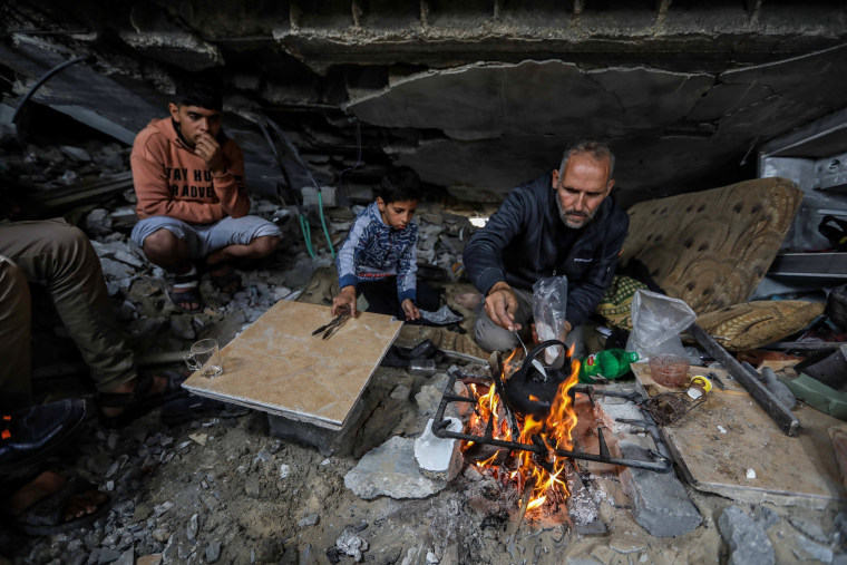 Palestinian Yassin Ahmed Al-Qara, 47, sits with his family under the rubble of his destroyed house on Nov. 28, 2023 in Khan Younis, southern Gaza.