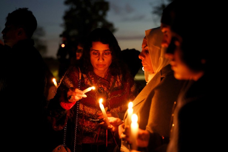 A woman uses a candle to ignite additional candles held by vigil attendees