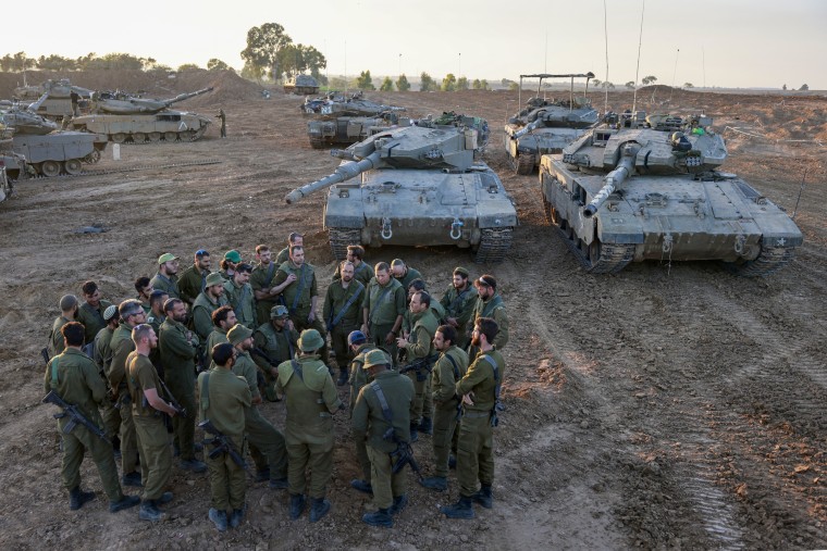 Israeli soldiers deployed on the southern border with the Gaza Strip on Nov. 29, 2023, gather for a briefing next to battle tanks.