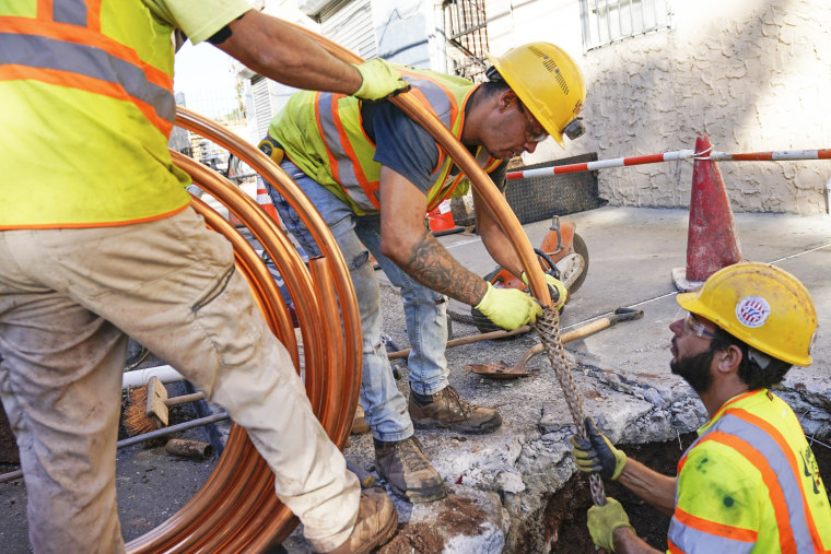 Construction employees in yellow vests work in sidewalk opening as they replace pipes