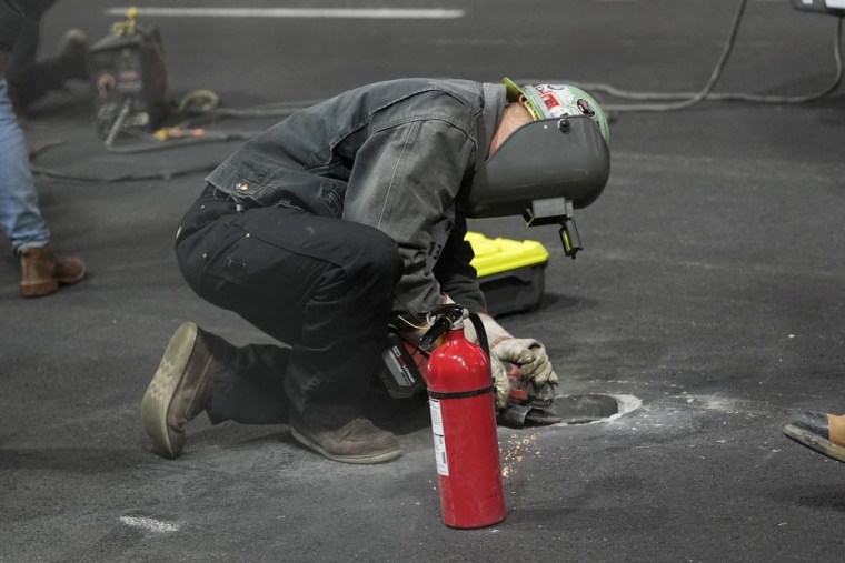 Un trabajador arregla la tapa que daño el Ferrari de Carlos Sainz, Jr., en Las Vegas.
