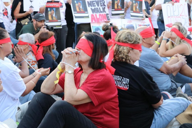 Demonstrators sit wearing red blindfolds with their hands zip-tied in Tel Aviv today.