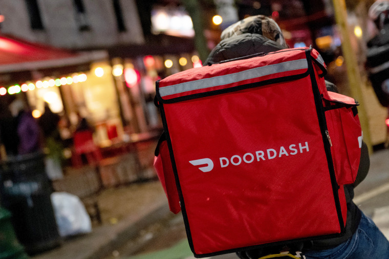 A door-dash delivery driver waits near a restaurant.