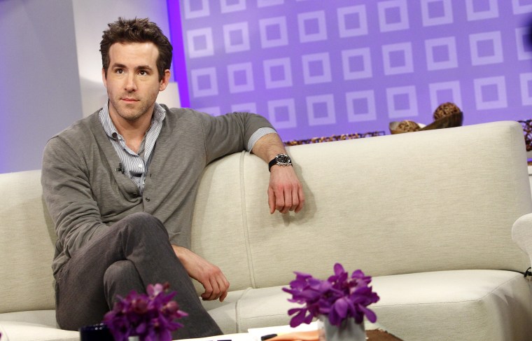 Reynolds in a grey cardigan sits on a white couch on the set of TODAY.
