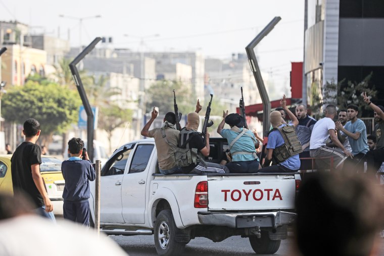 Militants with guns sit in the back of a pick up truck as it drives through a street